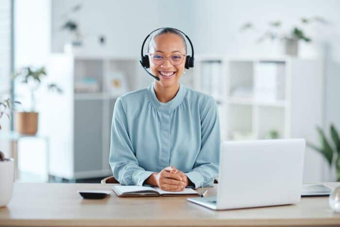 ai call center agent - Happy and confident call center agent sitting in front of a laptop while wearing a headset in an of