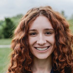 Bright smiling woman with red curly hair outdoors in a green park setting, showcasing happiness and natural beauty for AI Dial Australian business branding and communication solutions.