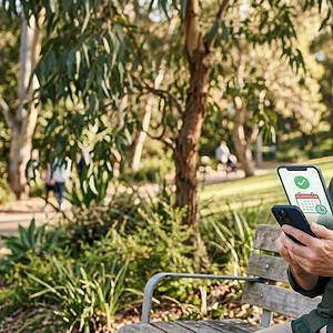 An older man sitting on a park bench using a smartphone with the AiDial app displayed on the screen, surrounded by trees and greenery, demonstrating mobile accessibility and communication technology.