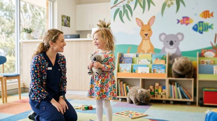 A caregiver and young girl smiling and playing together in a colorful childcare center with toys, books, and animal-themed wall decor, promoting a friendly and nurturing environment.
