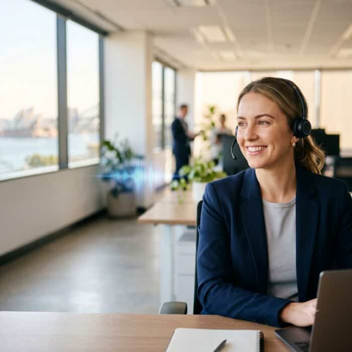 Professional woman customer service agent wearing a headset, working at her desk in a modern office environment, providing support and assistance to clients.