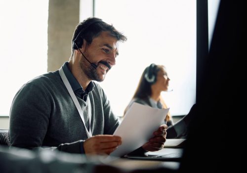 Happy call center agent with headset using laptop in the office.